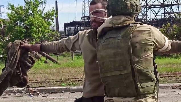 Captura de um frame de vídeo feito em 17 de maio de 2022 e divulgado pelo Ministério da Defesa da Rússia, mostra um membro do serviço ucraniano sendo revistado por um oficial militar russo, depois de deixar a siderúrgica Azovstal sitiada na cidade portuária de Mariupol, na Ucrânia.