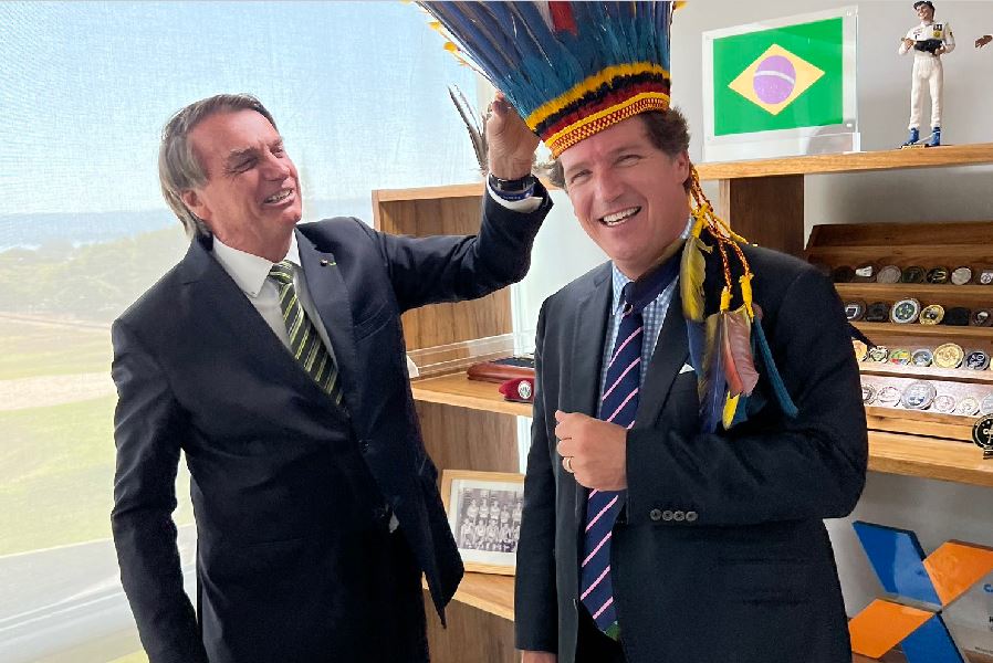 O presidente Jair Bolsonaro (PL) e o jornalista Tucker Carlson, da Fox News: cocar, Piquet e logo da Caixa