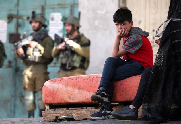 Uma criança palestina sentada `a frente de soldados israelenses durante confrontos com palestinos no centro da cidade de Hebron, Cisjordânia, em 2021.