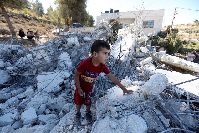 Uma criança palestina nos escombros de um prédio em construção danificado após a demolição de escavadeiras israelenses na vila de Biet Ommar, na Cisjordânia, ao norte de Hebron.
