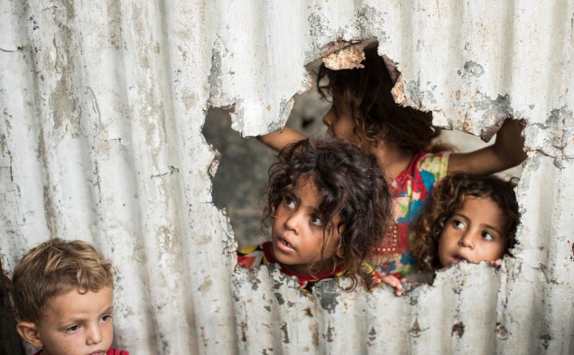 Crianças palestinas olham através de um buraco de uma cerca de metal, em um bairro pobre da Cidade de Gaza, em 8 de agosto de 2021.