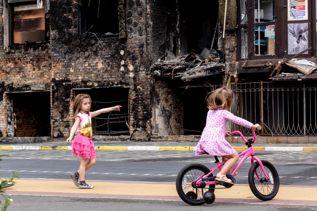 Two girls are seen in front a residential area affected by bombardment - June 14, 2022 in Bucha, Ukraine. As the Russian Federation invaded Ukraine more than 3 and a half months ago, fierce fighting continues in the East of the country. Some of the most devastated towns since the beginning of the conflict - Irpin and Bucha - build their way to normality. More and more civilians get back to their homes and reestablish their lives. (Photo by Dominika Zarzycka/NurPhoto via Getty Images)
