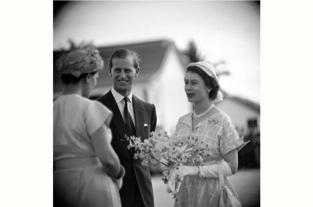Uma mulher cumprimentando a rainha Elizabeth II e o príncipe Philip e lhe oferece um buquê de flores. Anos 60.