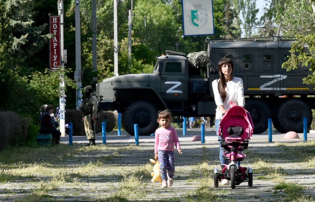 Uma mulher e uma criança andando em um parque enquanto militares russos patrulham a rua em Skadovsk, Kherson Oblast, em meio à ação militar russa em andamento na Ucrânia, em 25/05/2022.