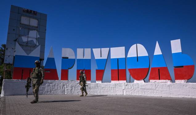 Militares russos caminham perto da placa de boas-vindas "Mariupol", com as cores da bandeira russa, em 12 de junho de 2022.