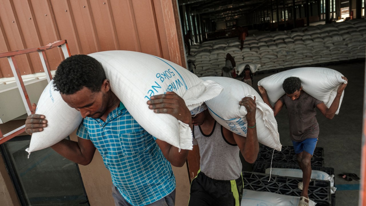 Workers carry sacks of grain in a warehouse of the World Food Programme (WFP) in the city of Abala, Ethiopia, on June 9, 2022. - The Afar region, the only passageway for humanitarian convoys bound for Tigray, is itself facing a serious food crisis, due to the combined effects of the conflict in northern Ethiopia and the drought in the Horn of Africa which have notably caused numerous population displacements. More than a million people need food aid in the region according to the World Food Programme. (Photo by EDUARDO SOTERAS / AFP)