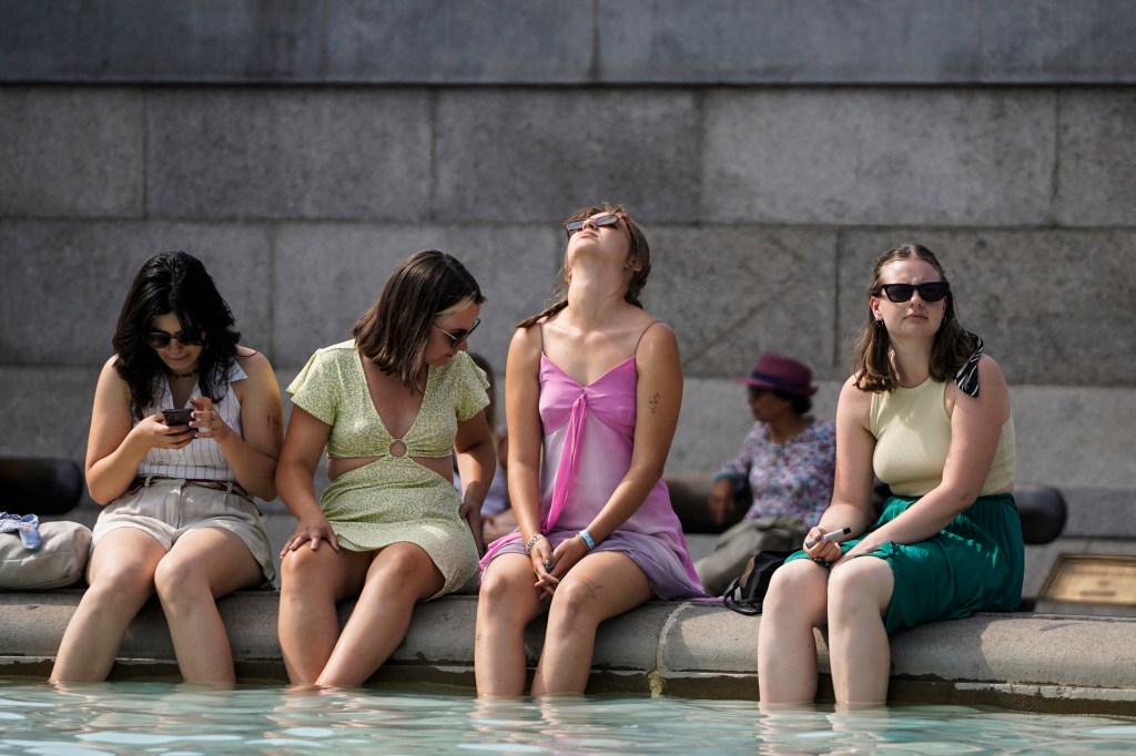A group of women cool off by dipping their feet in the fountain of Trafalgar Square, in central London, on July 18, 2022 as the country experiences an extreme heat wave. - Britain could hit 40 Celsius (104 Fahrenheit) for the first time, forecasters said, causing havoc in a country unprepared for the onslaught of extreme heat that authorities said was putting lives at risk. (Photo by Niklas HALLE'N / AFP)