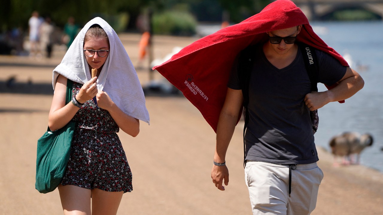 People cover their heads to shelter from the sun as they walk past the Serpentine lake in Hyde Park, west London, on July 19, 2022 as the country experiences an extreme heat wave. - Britain could hit 40 Celsius (104 Fahrenheit) for the first time, forecasters said, causing havoc in a country unprepared for the onslaught of extreme heat that authorities said was putting lives at risk. (Photo by Niklas HALLE'N / AFP)