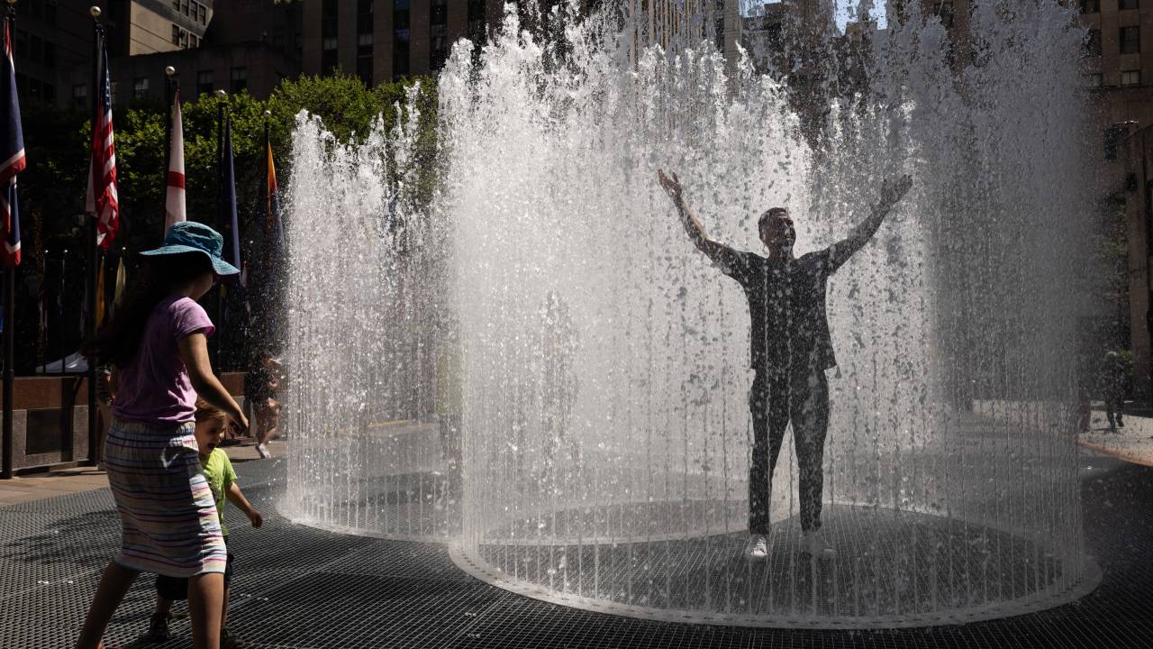 People play in the water-based sculpture of artist Jeppe Hein titled "Changing Spaces" at Rockefeller Center Plaza in New York City on July 19, 2022, as a heat wave continues throughout Europe and North America. (Photo by Yuki IWAMURA / AFP)