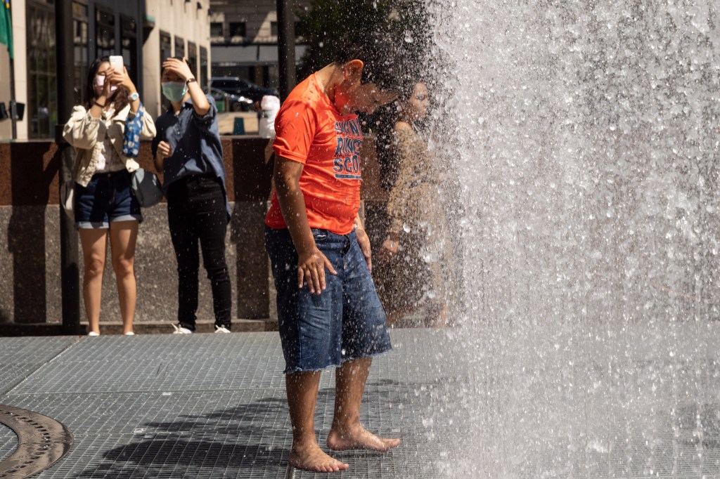 People play in the water-based sculpture of artist Jeppe Hein titled "Changing Spaces" at Rockefeller Center Plaza in New York City on July 19, 2022, as a heat wave continues throughout Europe and North America. (Photo by Yuki IWAMURA / AFP)