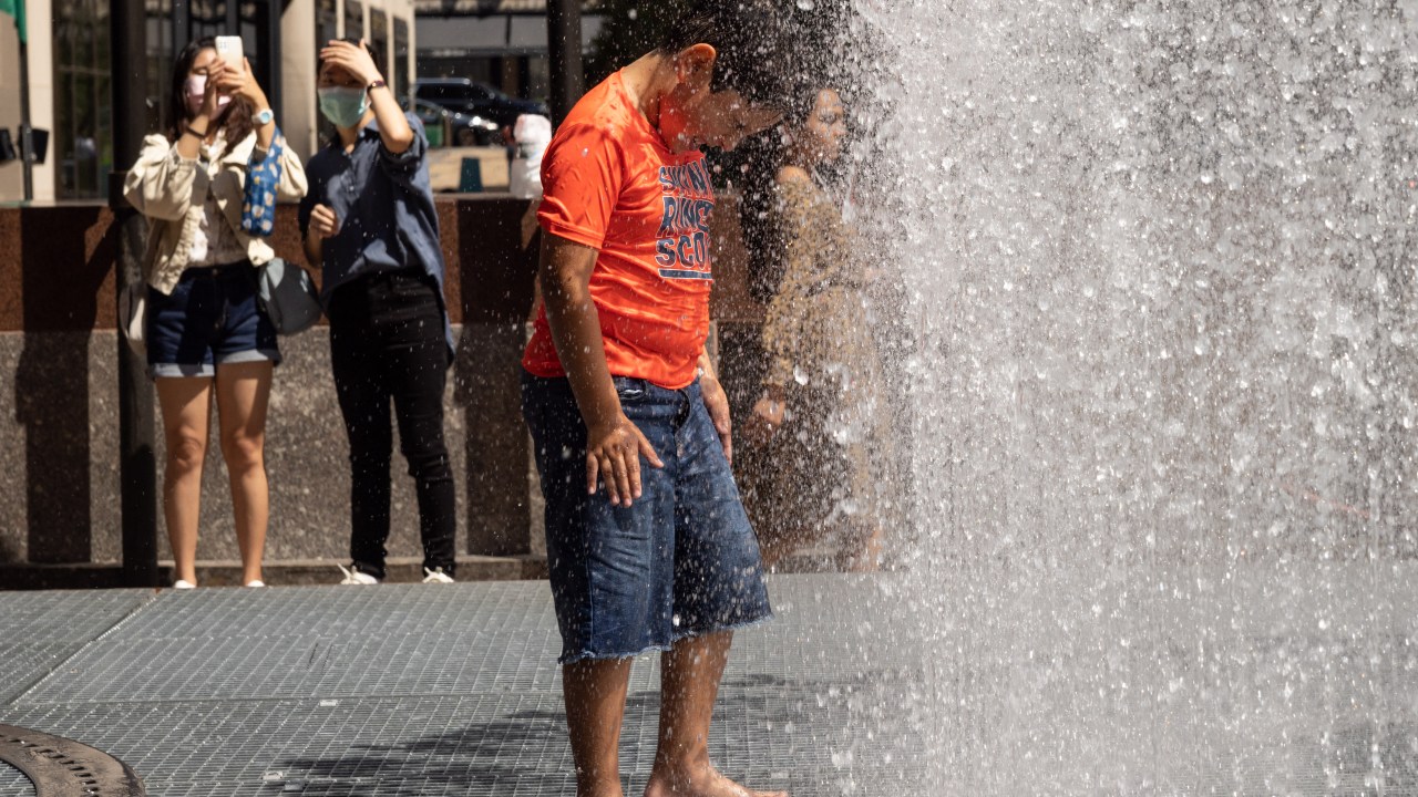 People play in the water-based sculpture of artist Jeppe Hein titled "Changing Spaces" at Rockefeller Center Plaza in New York City on July 19, 2022, as a heat wave continues throughout Europe and North America. (Photo by Yuki IWAMURA / AFP)