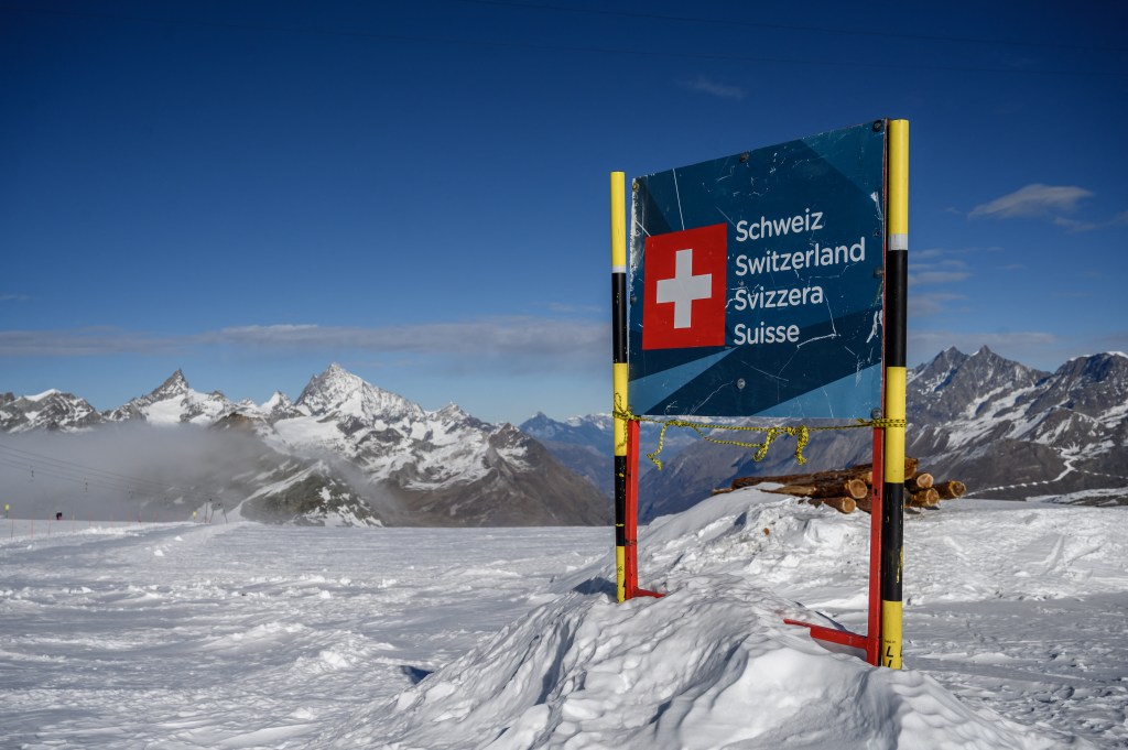 photograph taken on November 28, 2020 shows a banner marking the Swiss border near the 3,480-metre high Rifugio Guide del Cervino refuge at Testa Grigia peak between Zermatt Switzerland and Breuil-Cervinia, Italy. - Way up in the snowy Alps, the border between Switzerland and Italy has shifted due to a melting glacier, putting the location of an Italian mountain refuge in dispute. The border line runs along the drainage divide -- the point at which meltwater will run off down either side of the mountain towards one country or the other. But the Theodul Glacier's retreat means the watershed has crept towards the Rifugio Guide del Cervino, by the 3,480-metre high Testa Grigia peak -- and is gradually sweeping underneath the building. (Photo by Fabrice COFFRINI / AFP)