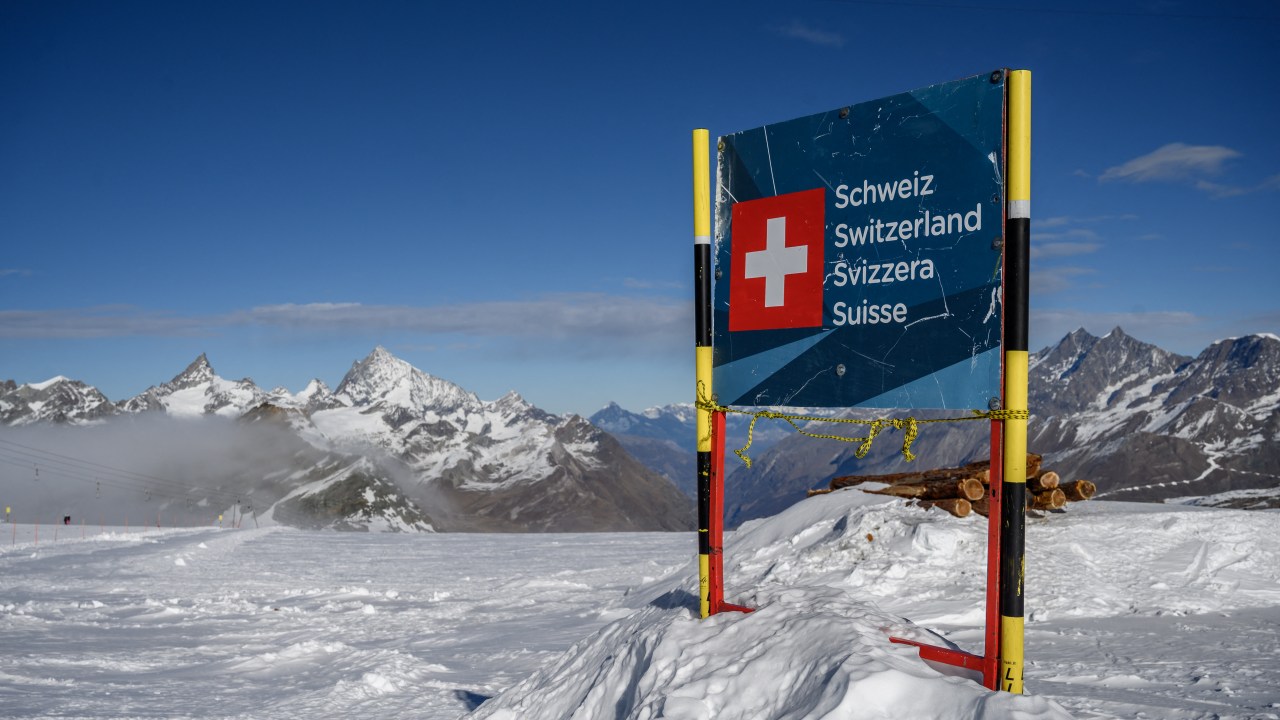 photograph taken on November 28, 2020 shows a banner marking the Swiss border near the 3,480-metre high Rifugio Guide del Cervino refuge at Testa Grigia peak between Zermatt Switzerland and Breuil-Cervinia, Italy. - Way up in the snowy Alps, the border between Switzerland and Italy has shifted due to a melting glacier, putting the location of an Italian mountain refuge in dispute. The border line runs along the drainage divide -- the point at which meltwater will run off down either side of the mountain towards one country or the other. But the Theodul Glacier's retreat means the watershed has crept towards the Rifugio Guide del Cervino, by the 3,480-metre high Testa Grigia peak -- and is gradually sweeping underneath the building. (Photo by Fabrice COFFRINI / AFP)