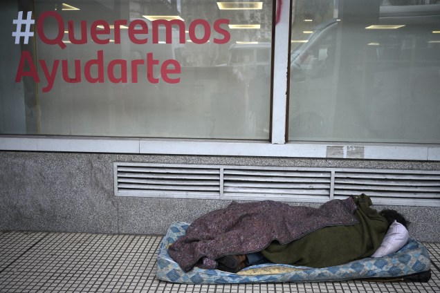 Uma pessoa dorme na calçada em frente `a um banco, com uma frase "Queremos ajudá-lo", no centro de Buenos Aires, em 11/07/2022.