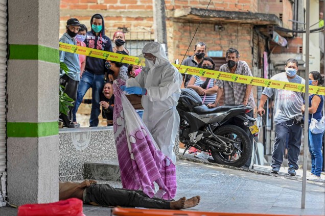 Um policial vestindo um traje de proteção examina um corpo de um homem que morreu na rua em Medellín, Colômbia, em 06/05/2020 em meio à pandemia de coronavírus Covid-19. Um policial vestindo um traje de proteção examina um corpo de um homem que morreu na rua em Medellín, Colômbia, em 06/05/2020 em meio à pandemia de coronavírus Covid-19.