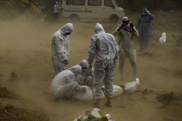 Parentes usando equipamentos de proteção amarram o corpo de uma vítima que morreu do coronavírus COVID-19 antes do enterro em um cemitério em Nova Déli, 10/05/2020.