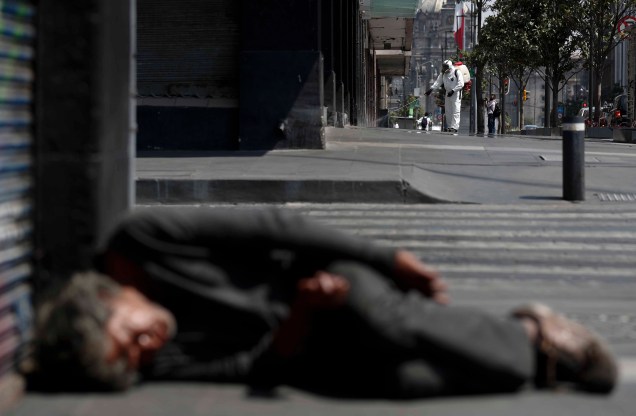 Um funcionário de saúde pulveriza desinfetante enquanto um homem dorme na rua, no centro da Cidade do México, em 06/04/2020. Um funcionário de saúde pulveriza desinfetante enquanto um homem dorme na rua, no centro da Cidade do México, em 06/04/2020.