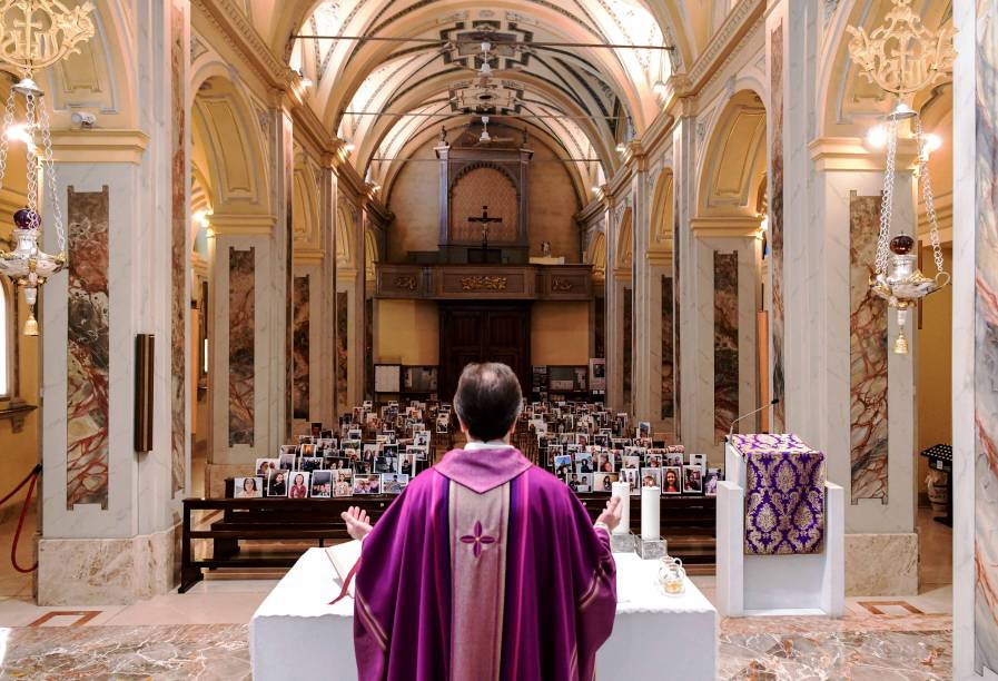 Don Giuseppe Corbari, pároco da Igreja de Robbiano, celebra a missa dominical enquanto olha para fotos de selfie enviadas por membros de sua paróquia e coladas em bancos vazios em Giussano, Itália em 22/03/2020.