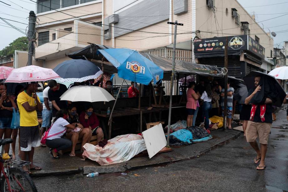 Moradores vigiam vários corpos cobertos com diversos panos na favela do Alemão, no Rio de Janeiro, Brasil, 15/05/2020.  (Foto AP/Leo Correa)