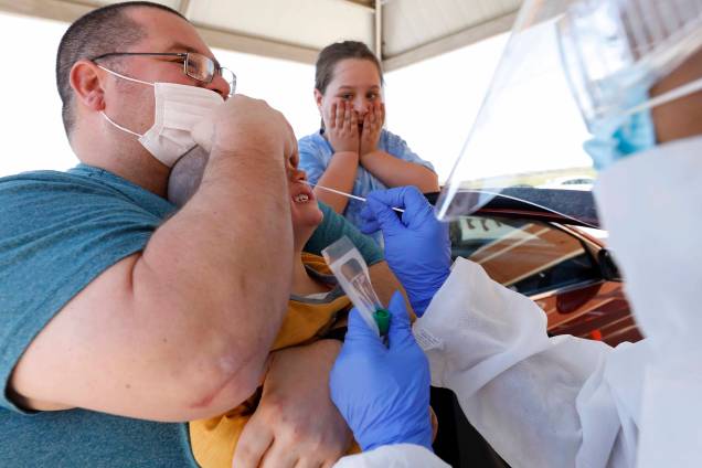 Pai segura seu filho enquanto realiza teste de cotonete nasal por um dos funcionários do Delta Health Center em uma unidade de teste gratuito de COVID-19 no Centro Médico Dr. H. Jack Geiger, em Mound Bayou, Mississippi, 16/04/2020.