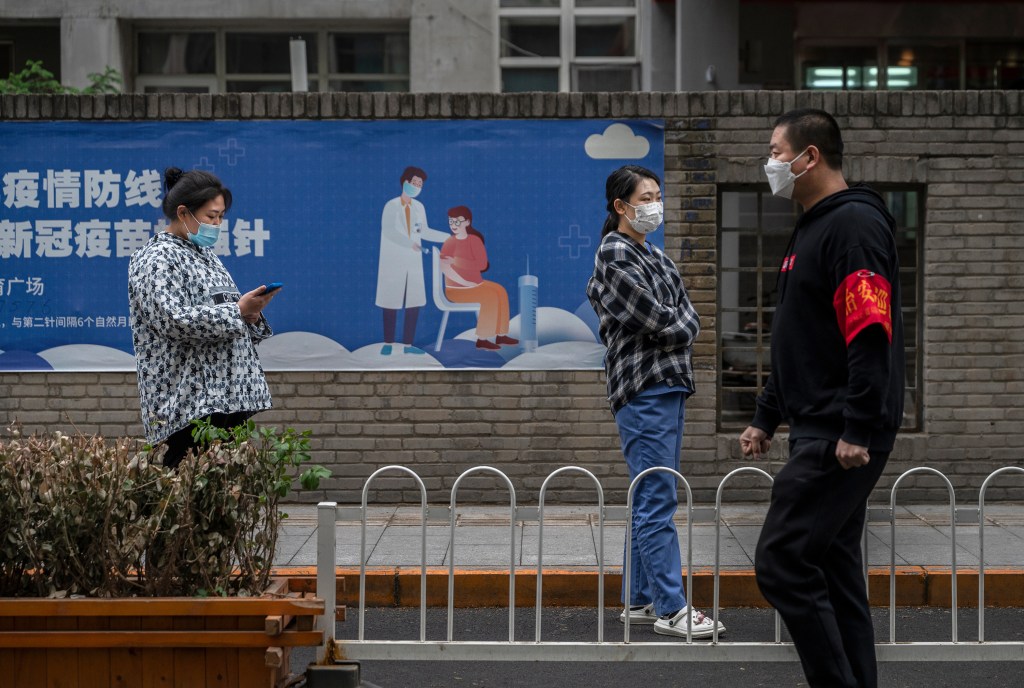 BEIJING, CHINA - APRIL 27: People wait in line for nucleic acid tests to detect COVID-19 next to a poster for vaccinations at a makeshift testing site in the Central Business District in Chaoyang on April 27, 2022 in Beijing, China. China is trying to contain a spike in coronavirus cases in the capital Beijing after dozens of people tested positive for the virus in recent days, causing local authorities to initiate mass testing in most districts and to lockdown some neighbourhoods where cases are found in an effort to maintain the country's zero COVID strategy. (Photo by Kevin Frayer/Getty Images)