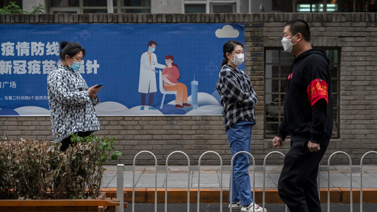 BEIJING, CHINA - APRIL 27: People wait in line for nucleic acid tests to detect COVID-19 next to a poster for vaccinations at a makeshift testing site in the Central Business District in Chaoyang on April 27, 2022 in Beijing, China. China is trying to contain a spike in coronavirus cases in the capital Beijing after dozens of people tested positive for the virus in recent days, causing local authorities to initiate mass testing in most districts and to lockdown some neighbourhoods where cases are found in an effort to maintain the country's zero COVID strategy. (Photo by Kevin Frayer/Getty Images)