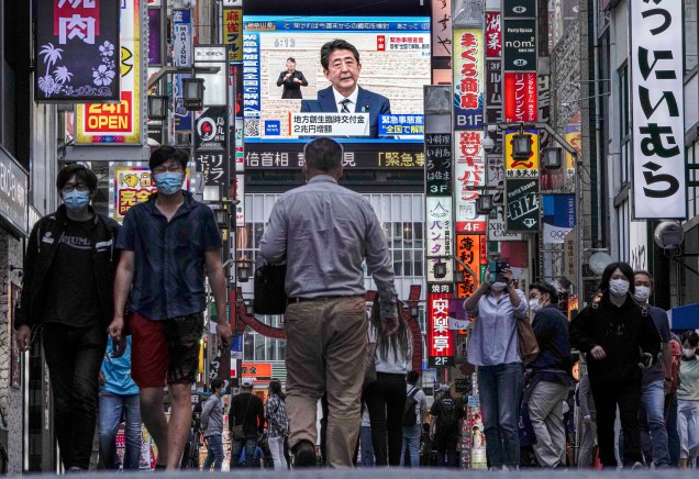 Pessoas caminham por uma rua de Kabukicho, o maior distrito de entretenimento noturno do Japão em Shinjuku em Tóquio, na TV o ex primeiro-ministro japonês Shinzo Abe suspende o estado de emergência no país, após uma queda nos casos de coronavírus. 25/05/2020.