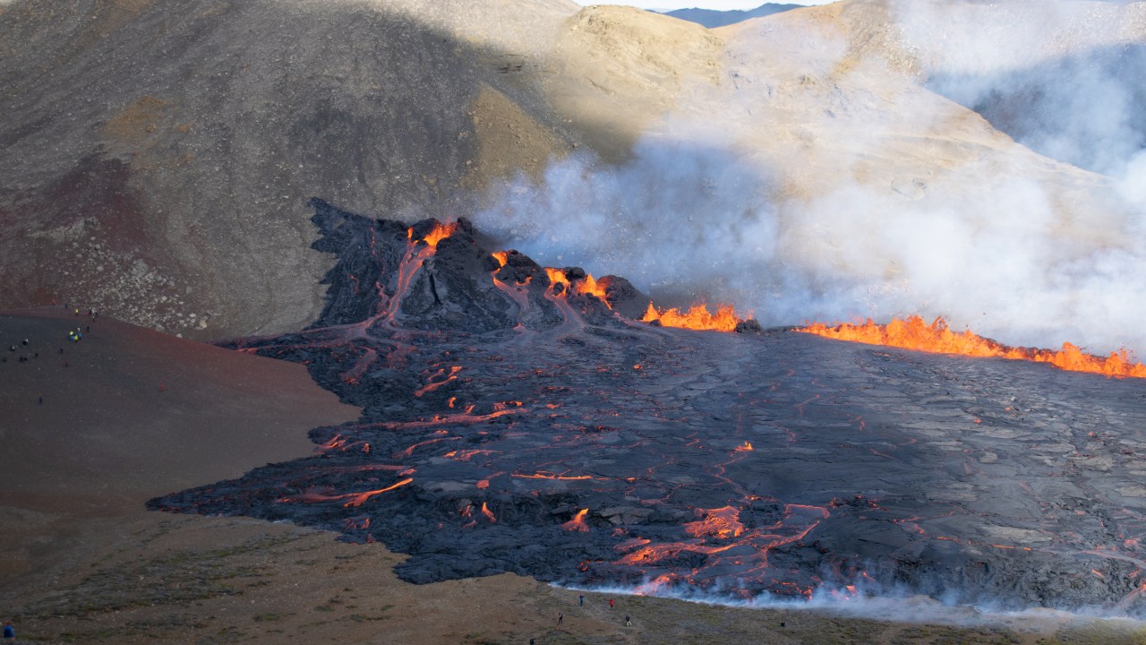 People look at the lava flowing at the scene of the newly erupted volcano at Grindavik, Iceland on August 3, 2022. - A volcano erupted on August 3, 2022 in Iceland in a fissure near Reykjavik, the Icelandic Meteorological Office (IMO) said as lava could be seen spewing out of the ground in live images on local media. The eruption was some 40 kilometres (25 miles) from Reykjavik, near the site of the Mount Fagradalsfjall volcano that erupted for six months in March-September 2021, mesmerising tourists and spectators who flocked to the scene. (Photo by Jeremie RICHARD / AFP)