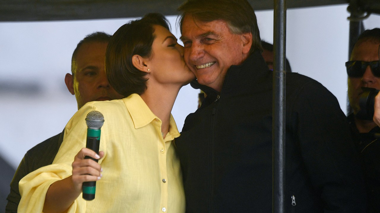 Brazil's President Jair Bolsonaro is kissed by his wife Michelle Bolsonaro during the launching of his re-election campaign for the upcoming national elections in October, in Juiz de Fora, Minas Gerais state, Brazil, on August 16, 2022. - Bolsonaro, 67, launched his campaign with a rally in Juiz de Fora, the small southeastern city where an attacker stabbed and nearly killed him during his 2018 campaign. The attack cemented Bolsonaro in the minds of die-hard supporters as "The Myth" -- a hero swooping in to rough up the political establishment and speak his mind with tough-talking clarity. (Photo by MAURO PIMENTEL / AFP)