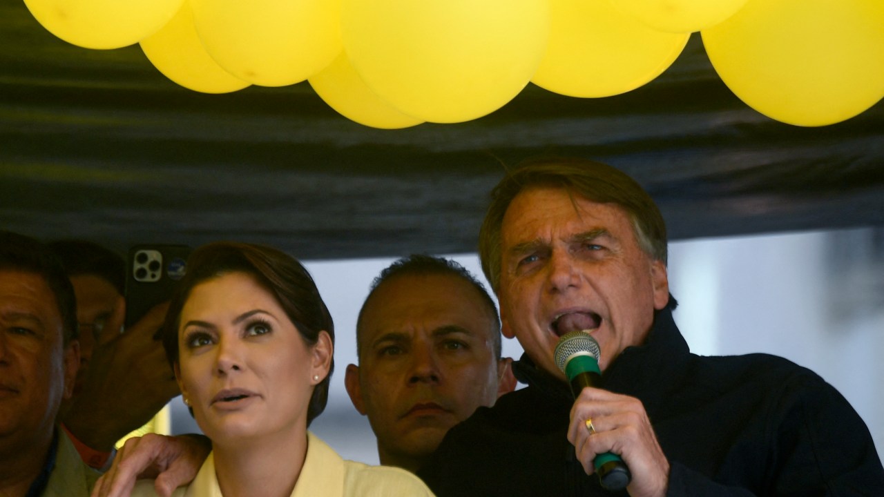 Brazil's President Jair Bolsonaro speaks next to his wife Michelle Bolsonaro during the launching of his re-election campaign for the upcoming national elections in October, in Juiz de Fora, Minas Gerais state, Brazil, on August 16, 2022. - Bolsonaro, 67, launched his campaign with a rally in Juiz de Fora, the small southeastern city where an attacker stabbed and nearly killed him during his 2018 campaign. The attack cemented Bolsonaro in the minds of die-hard supporters as "The Myth" -- a hero swooping in to rough up the political establishment and speak his mind with tough-talking clarity. (Photo by MAURO PIMENTEL / AFP)