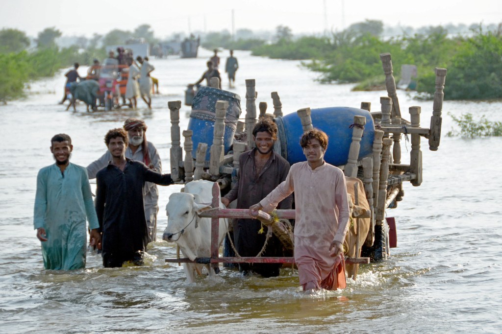 Stranded people along with their belongings wade through a flooded street after fleeing from their flood hit homes following heavy monsoon rains at Sohbatpur area in Jaffarabad district of Balochistan province on August 28, 2022. - Pakistan's flooded southern Sindh province braced on August 28 for a fresh deluge from swollen rivers in the north as the death toll from this year's monsoon topped 1,000. (Photo by Fida HUSSAIN / AFP)