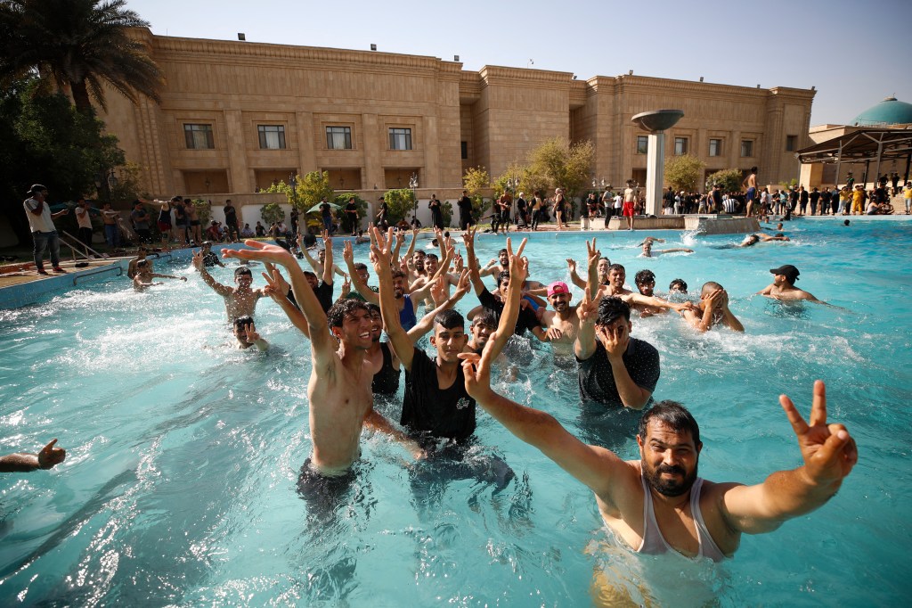 Supporters of Iraqi Shiite cleric Moqtada Sadr swim in the pool of the Government Headquarters in the capital Baghdad's Green Zone, on August 29, 2022. - Dozens of angry supporters of the powerful cleric stormed the Republican Palace, a ceremonial building in the fortified Green Zone, a security source said, shortly after Sadr said he was quitting politics. The army has announced a Baghdad-wide curfew to start from 3:30 pm (1230 GMT). (Photo by Ahmad Al-rubaye / AFP)