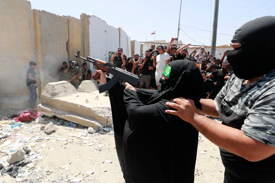 Um membro armado da Brigada da Paz, ala militar afiliada ao clérigo xiita Moqtada al-Sadr, ajuda uma mulher a disparar uma metralhadora durante confrontos com forças de segurança iraquianas na Zona Verde de Bagdá, capital do Iraque - 30/08/2022 -