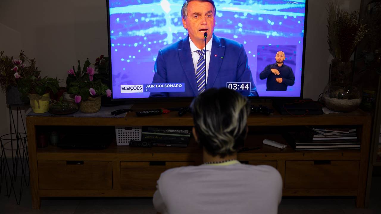 AME2399. BRASILIA (BRASIL), 28/08/2022.- Una mujer mira por televisión el primer debate de las elecciones presidenciales de 2022 en Brasilia (Brasil). El presidente brasileño, Jair Bolsonaro, atacó este domingo a su principal rival en las elecciones, el expresidente Luiz Inácio Lula da Silva, sacando a relucir la corrupción en su Gobierno, durante el primer debate de la campaña. EFE/ Joédson Alves.
