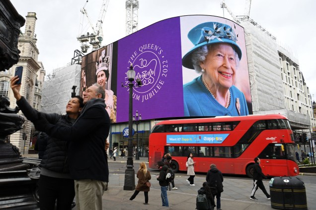 Um casal tira uma selfie enquanto as imagens da rainha Elizabeth II da Grã-Bretanha são exibidas -