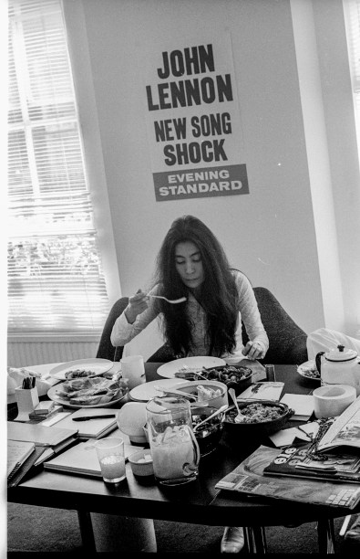 Yoko Ono almoçando comida macrobiótica no escritório da Apple Corps, em Savile Row, em Londres. No canto direito da mesa estão exemplares de revistas da editora Manchete -