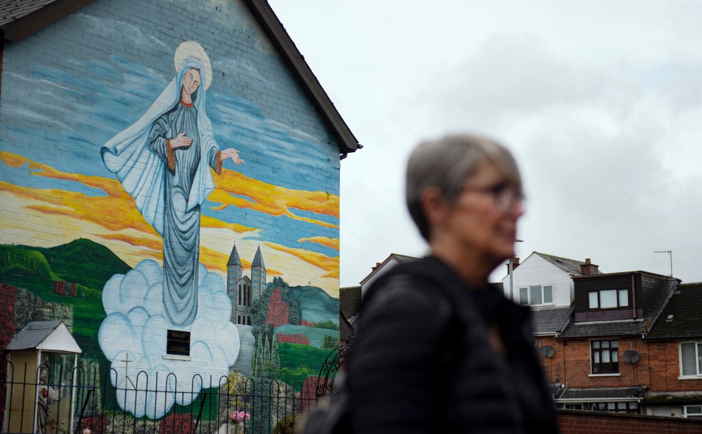 BELFAST, NORTHERN IRELAND - SEPTEMBER 22: A woman walks past a Catholic religious mural on the day that the Northern Ireland census was released on September 22, 2022 in Belfast, Northern Ireland. The latest census figures show that for the first time in Northern Irelands 101-year history there are more people from a Catholic background in Northern Ireland than Protestant. The proportion of the resident population which is either Catholic is 45.7% compared to 43.48% Protestant. The previous census, in 2011, found that 45.1% of the population were Catholic compared to 48.4% who were from a Protestant or other Christian background. (Photo by Charles McQuillan/Getty Images)