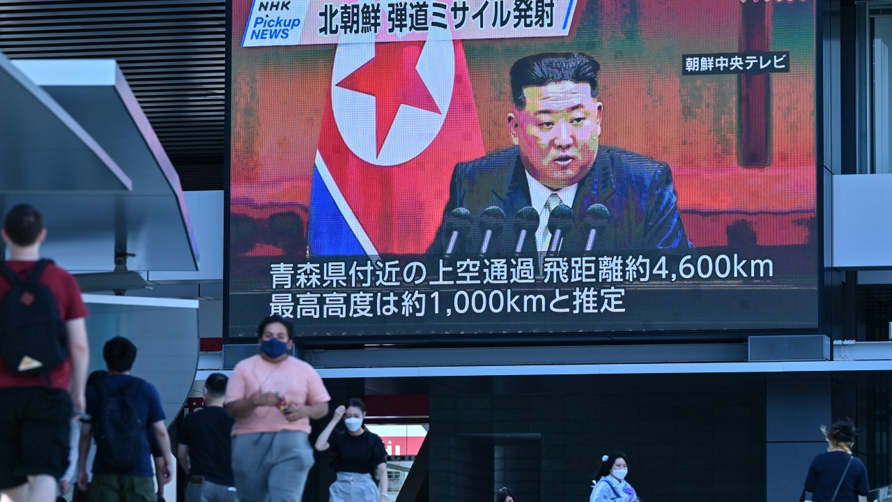 Pedestrians walk under a large video screen showing images of North Korea's leader Kim Jong Un during a news update in Tokyo on October 4, 2022, after North Korea launched a missile early in the day which prompted an evacuation alert when it flew over northeastern Japan. - North Korea fired a ballistic missile over Japan for the first time in five years on October 4, prompting Tokyo to activate its missile alert system and issue a rare warning for people to take shelter. (Photo by Richard A. Brooks / AFP)