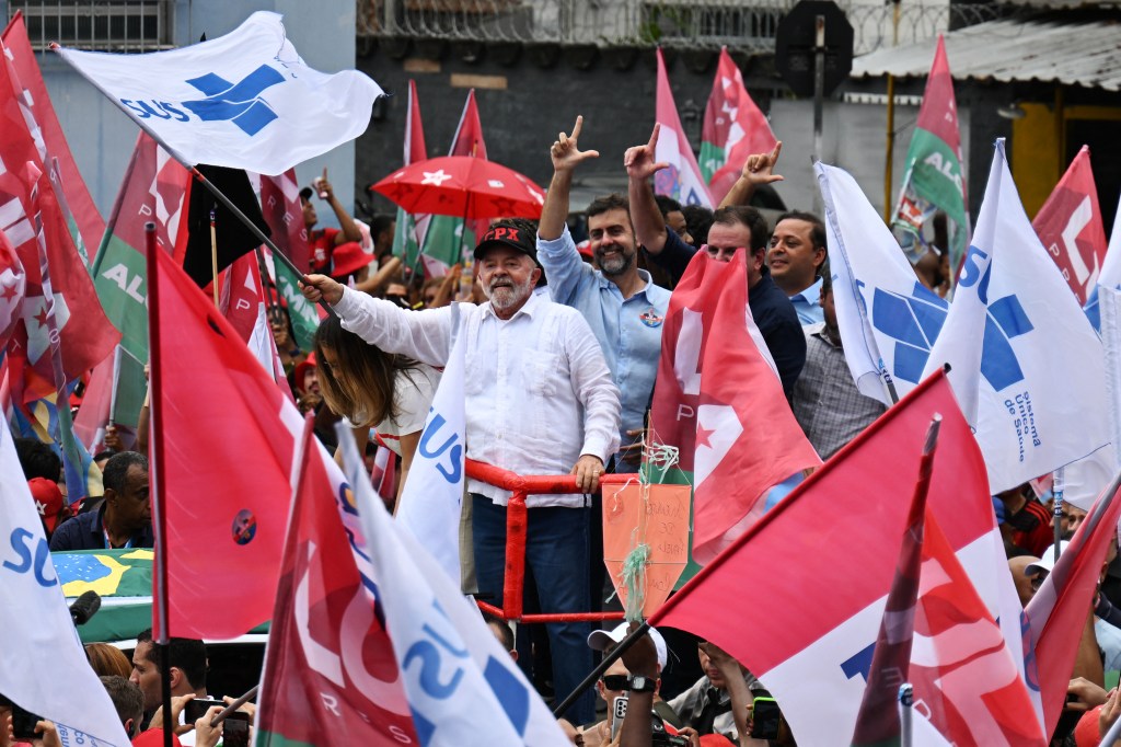 Brazilian former President (2003-2010) and presidential candidate for the leftist Workers Party (PT), Luiz Inacio Lula da Silva (C), greets his supporters during a rally at the Complexo do Alemao favela in Rio de Janeiro, Brazil, on October 12, 2022. - President Jair Bolsonaro, 67, exceeded polling predictions by coming a closer-than-expected second to ex-president Lula da Silva, 76, in a first election round on October 2. The two men will face off in a deeply polarized second round on October 30. (Photo by CARL DE SOUZA / AFP)