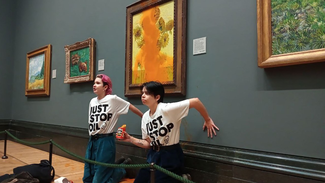 A handout picture from the Just Stop Oil climate campaign group shows activists with their hands glued to the wall under Vincent van Gogh's "Sunflowers" after throwing tomato soup on the painting at the National Gallery in central London on October 14, 2022. - London's Metropolitan Police said its officers arrested two protesters from the Just Stop Oil group for criminal damage and aggravated trespass after they "threw a substance over a painting" at the gallery on Trafalgar Square. (Photo by Handout / Just Stop Oil / AFP) / RESTRICTED TO EDITORIAL USE - MANDATORY CREDIT "AFP PHOTO / JUST STOP OIL " - NO MARKETING - NO ADVERTISING CAMPAIGNS - DISTRIBUTED AS A SERVICE TO CLIENTS