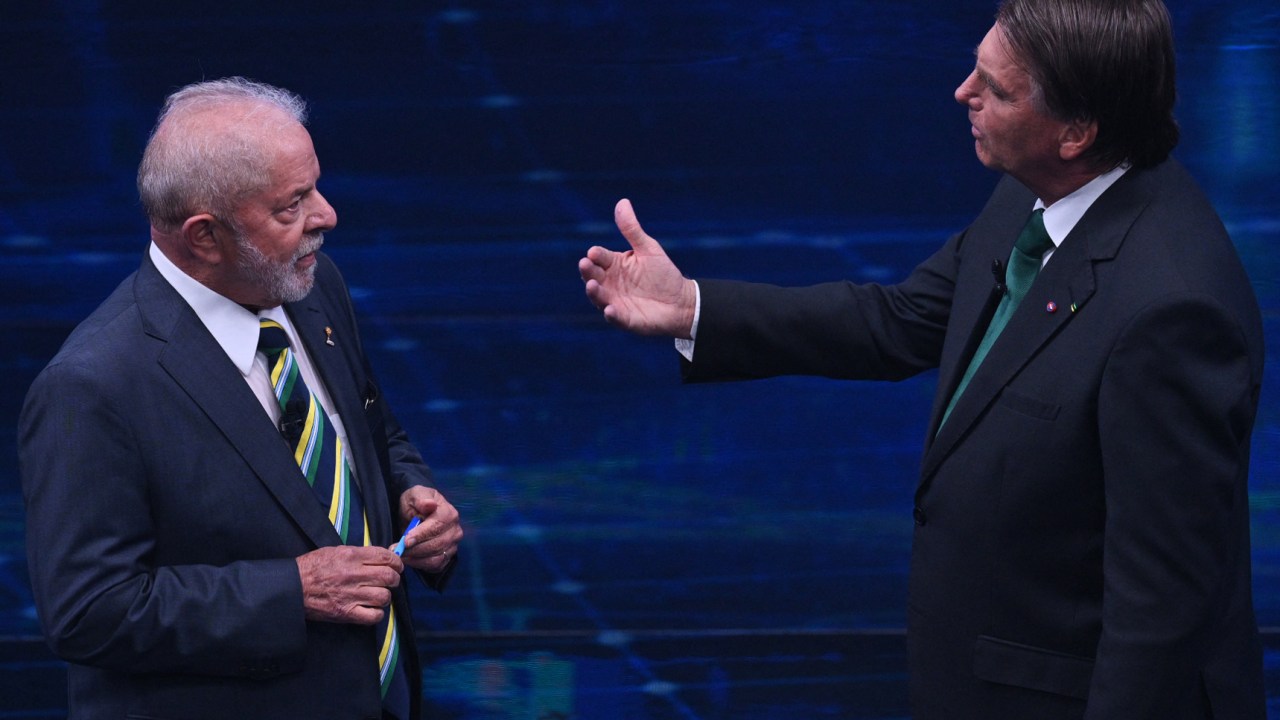 Brazilian former president (2003-2010) and presidential candidate for the leftist Workers Party (PT), Luiz Inacio Lula da Silva (L), and Brazilian President and presidential candidate Jair Bolsonaro (R) speak to each other during a televised presidential debate in Sao Paulo, Brazil, on October 16, 2022. - President Jair Bolsonaro and former President Luiz Inácio Lula da Silva face each other this Sunday night in the first face-to-face debate, in which they will try to take advantage 14 days before the second round of the presidential elections in Brazil. (Photo by NELSON ALMEIDA / AFP)