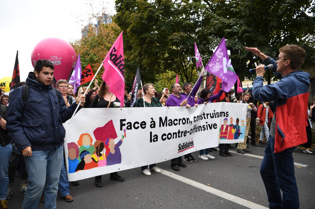 Protesters hold a sign reading 'Facing Macron, let's build the counter-offence' during a demonstration in Paris, on October 18, 2022 after the CGT and FO trade unions called for a nationwide strike for higher salaries, and against the government's requisitioning of fuel refineries to force some strikers back into opening fuel depots. - Unions in other industries and the public sector have also announced action to protest against the twin impact of soaring energy prices and overall inflation on the cost of living. (Photo by Bertrand GUAY / AFP)