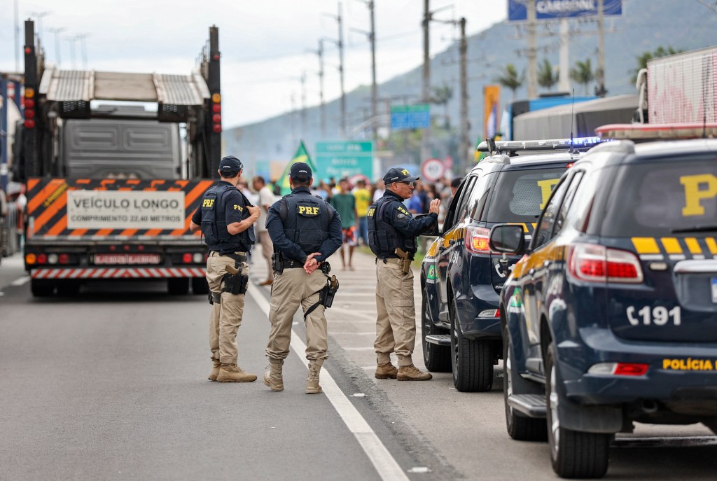 Members of the Federal Highway Police remain on the side of the road as supporters of President Jair Bolsonaro, mainly truck drivers, block BR-101 highway in Palhoca, in the metropolitan region of Florianopolis, Santa Catarina State, Brazil, on October 31, 2022, as an apparent protest over Bolsonaro's defeat in the presidential run-off election. - The transition period got off to a tense start as truckers and demonstrators blocked several highways across Brazil on Monday in an apparent protest over the electoral defeat of Bolsonaro to leftist Luiz Inacio Lula da Silva, burning tyres and parking vehicles in the middle of the road to halt traffic. (Photo by Anderson Coelho / AFP)