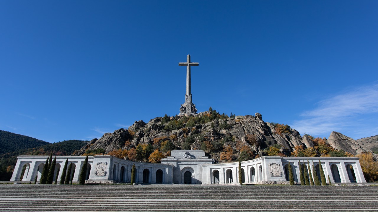 SAN LORENZO DE EL ESCORIAL MADR, SPAIN - NOVEMBER 18: General view of the monumental complex of the Valley of the Fallen, on 17 November 2021, in San Lorenzo de El Escorial, Madrid, Spain. The monumental complex of the Valley of the Fallen will return to its original name of Valley of Cuelgamuros, as indicated in one of the amendments agreed by PSOE and Unidas Podemos in the Law of Democratic Memory and also urges to relocate the remains buried there the founder of the Spanish Falange, Jose Antonio Primo de Rivera. The complex of the Valley of the Fallen consists of an abbey of the Benedictine order, a basilica and a monumental complex and is located in the Valley of Cuelgamuros. It was built mainly by the labour of Republican political prisoners. The cross, the tallest in the world, measures 150 meters. The monumental complex was ordered to be built in 1940 by Francisco Franco so that the founder of Primo de Rivera and the fallen of the so-called 'Glorious Crusade' could be buried there. Shortly before its inauguration in 1959 the remains of Republican soldiers were also buried there. In the end, 33,487 people were buried there, whose remains ended up forming part of the structure of the building itself. This makes the complex the 'largest mass grave in Spain', as established by the CSIC in 2018. Every November 20, the anniversary of Franco's death, the Valley of the Fallen becomes a place of pilgrimage for supporters of Franco and the dictator. (Photo By Rafael Bastante/Europa Press via Getty Images)
