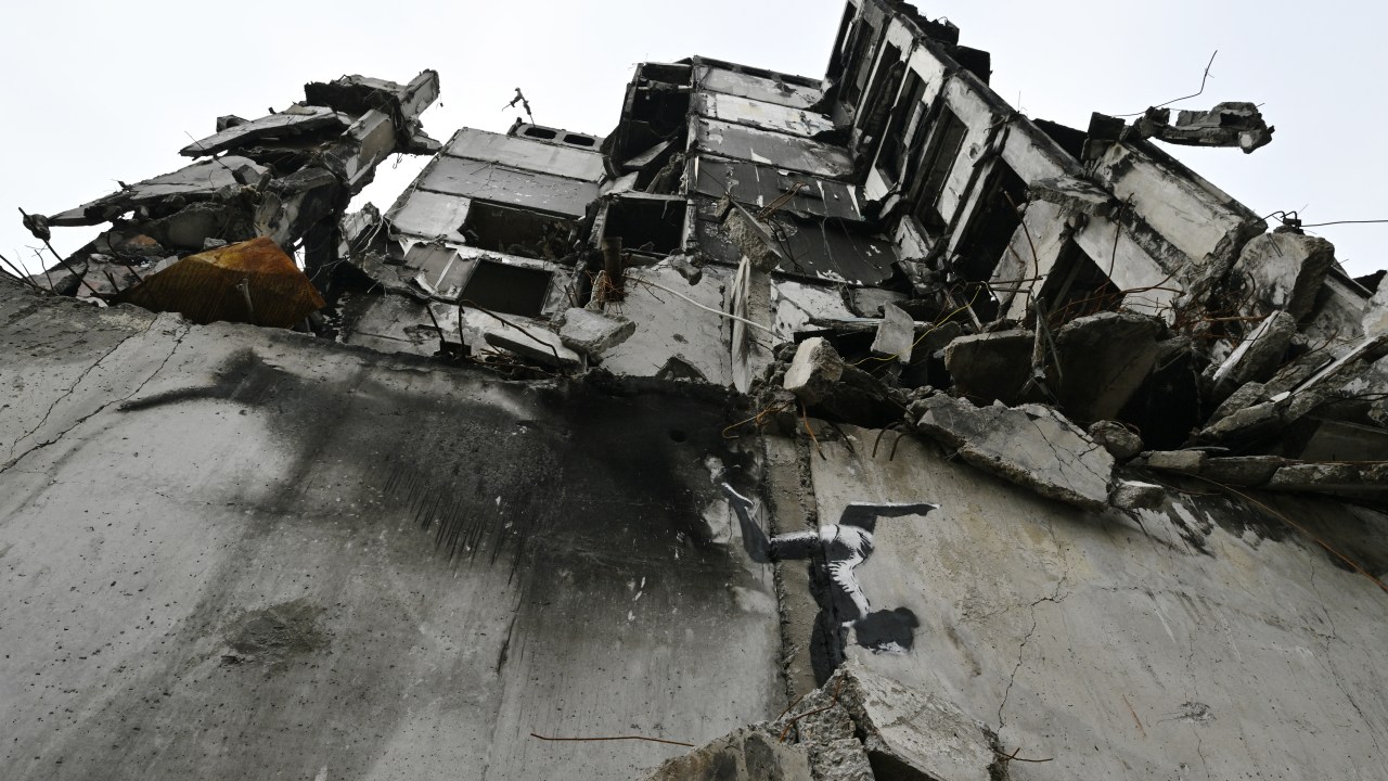 This photograph taken on November 12, 2022 shows a graffiti made by Banksy on the wall of a destroyed building in Borodyanka, near Kyiv, amid the Russian invasion of Ukraine. - Banksy, the elusive British street artist, has painted a mural on a bombed-out building outside Ukraine's capital, in what Ukrainians have hailed as a symbol of their country's invincibility. On November 11's night the world-famous graffiti artist posted on Instagram three images of the artwork -- a gymnast performing a handstand amid the ruins of a demolished building in the town of Borodyanka northwest of the Ukrainian capital Kyiv. (Photo by Genya SAVILOV / AFP) / RESTRICTED TO EDITORIAL USE - MANDATORY MENTION OF THE ARTIST UPON PUBLICATION - TO ILLUSTRATE THE EVENT AS SPECIFIED IN THE CAPTION