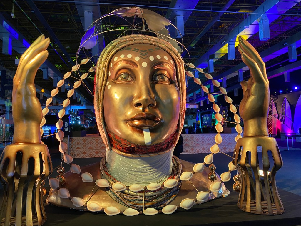 Escultura de uma figura feminina dourada que representa a logo da Segunda Expo Internacional da Consciência Negra