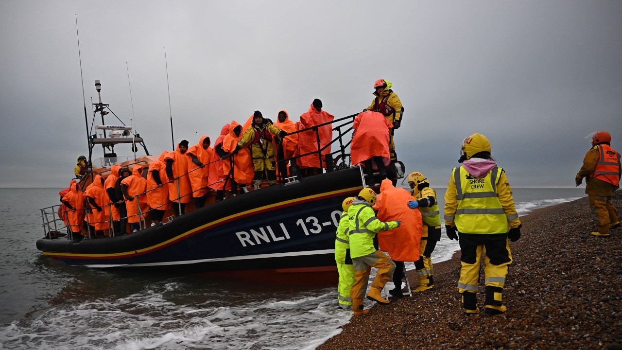 (FILES) In this file photo taken on December 9, 2022 migrants, picked up at sea attempting to cross the English Channel, are helped ashore from an Royal National Lifeboat Institution (RNLI) lifeboat, at Dungeness on the southeast coast of England. - UK high court judges ruled, on December 19, 2022 that the British government's controversial plan to deport migrants to Rwanda is lawful, after flights were thwarted through legal challenges by charities and asylum-seekers. In a bid to deal with the unprecedented number of arrivals, UK Prime Minister Rishi Sunak has sought to continue his predecessor Boris Johnson's scheme to deport migrants thousands of miles away to the African country. (Photo by Ben Stansall / AFP)