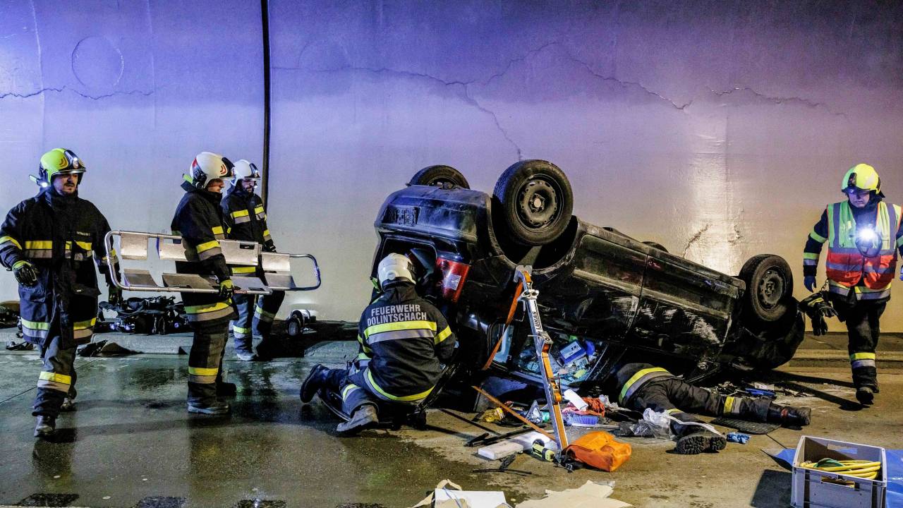 ÁUSTRIA - 2022/10/18: Bombeiros austríacos atendem uma vítima de acidente presa dentro de um carro capotado em um acidente de trânsito encenado durante um exercício de resgate internacional Karawanken 2022 no túnel transfronteiriço de tubo único entre a Eslovênia e a Áustria, perto de Sankt Jakob im Rosental. Em um exercício de resgate conjunto, equipes de resgate de bombeiros e ambulâncias de ambos os países responderam a um acidente de trânsito dentro de um túnel transfronteiriço entre a Eslovênia e a Áustria