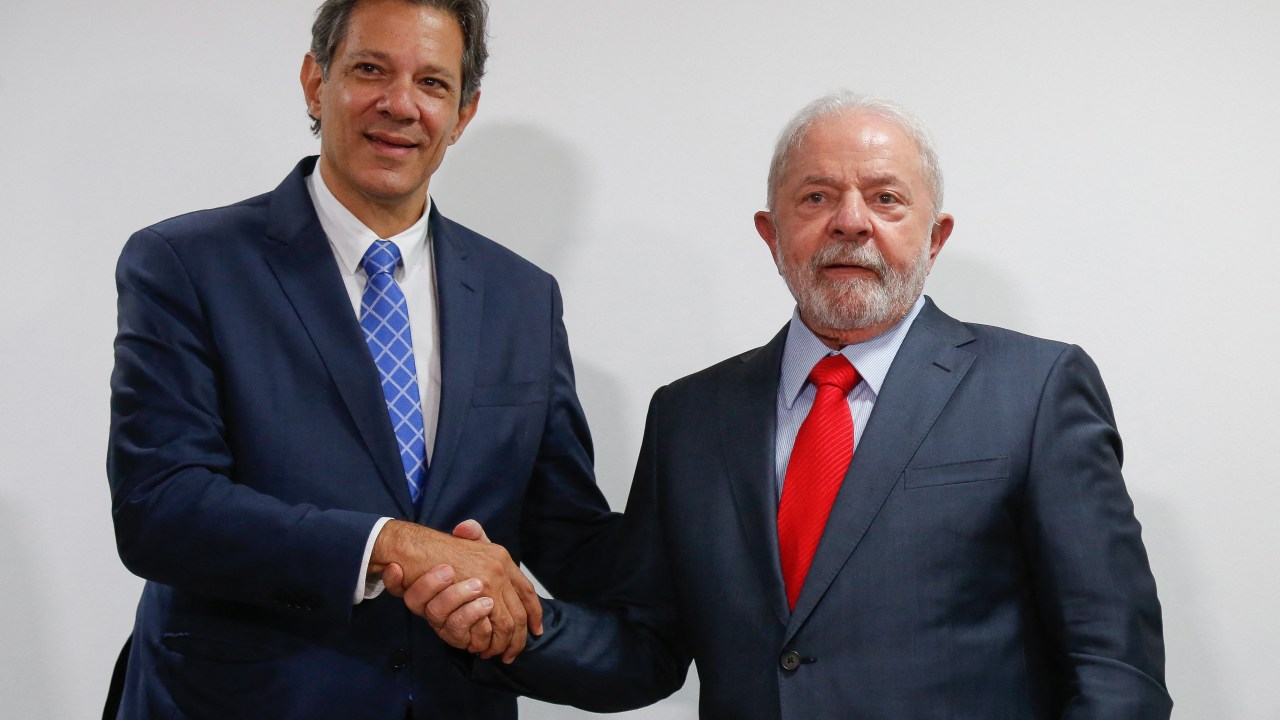Brazil's President Luiz Inacio Lula da Silva (R) and Finance Minister Fernando Haddad (L) shake hands during the presentation and signing of new economic measures at the Planalto Palace in Brasilia, on January 12, 2023. (Photo by Sergio Lima / AFP)