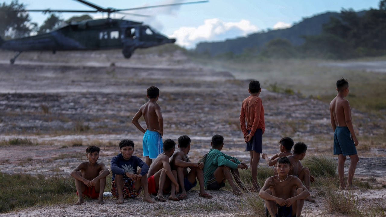 Yanomami indigenous men look at the movement of Brazil Air Force aircrafts at the Surucucu Airfield, located inside the Yanomami Territory, municipality of Alto Alegre, state of Roraima, Brazil, on January 28, 2023. - Cases of malnutrition and malaria in the region have skyrocketed in recent weeks, prompting the new leftist government of President Lula Inacio Lula da Silva to declare a health emergency. (Photo by MICHAEL DANTAS / AFP)